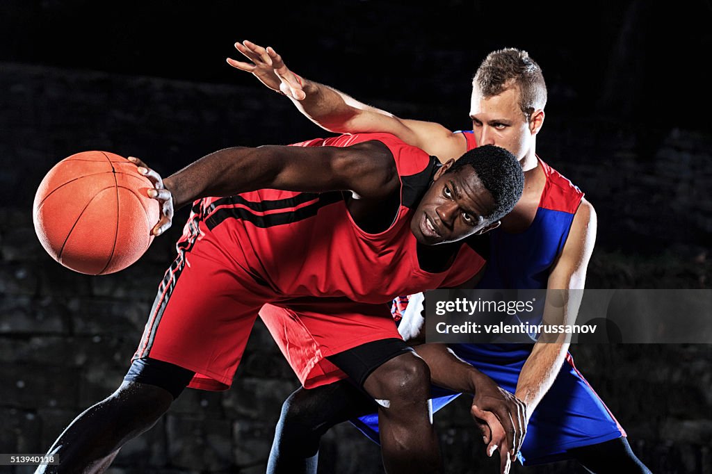 Caucasian and african basketball players in defence on black background