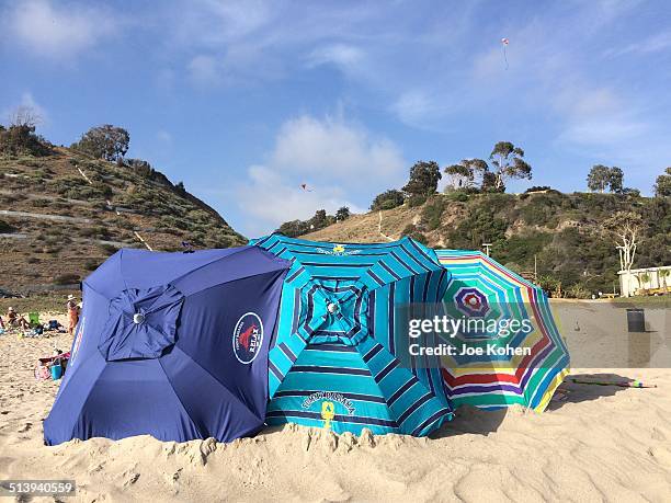 Three tilted parasols laid down protecting beach goers during a windy day on the Santa Monica beach in California.