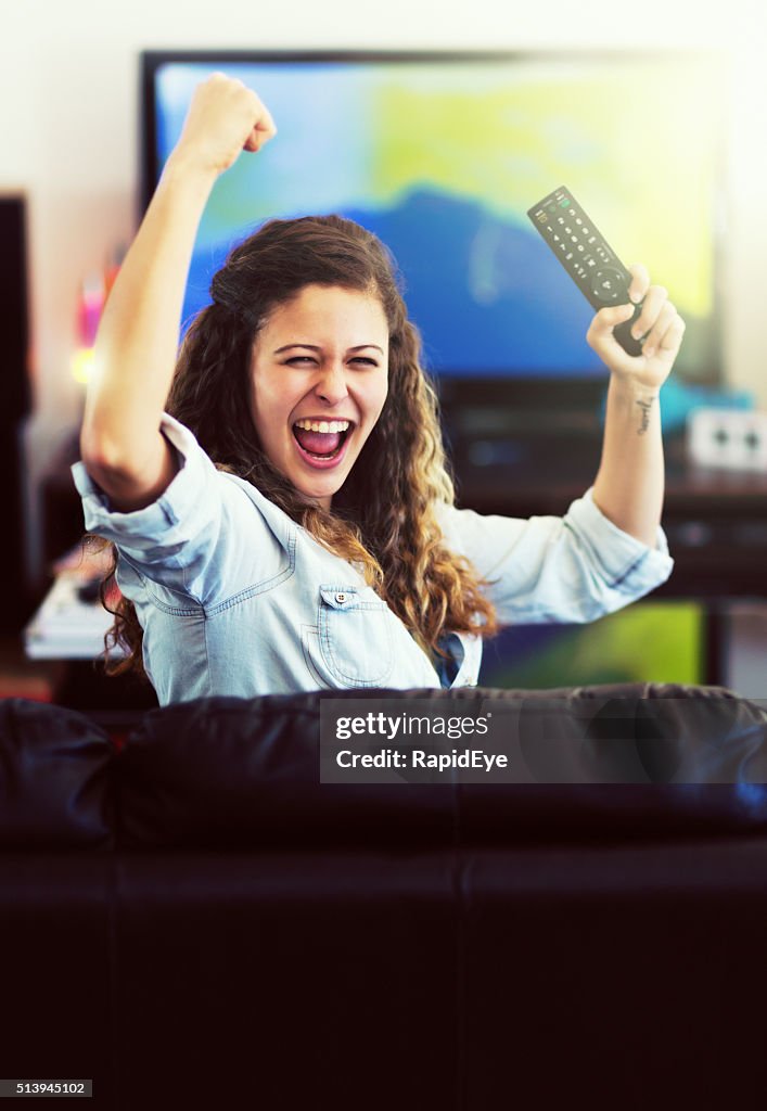 Pretty sports enthusiast holds TV remote, cheering her team