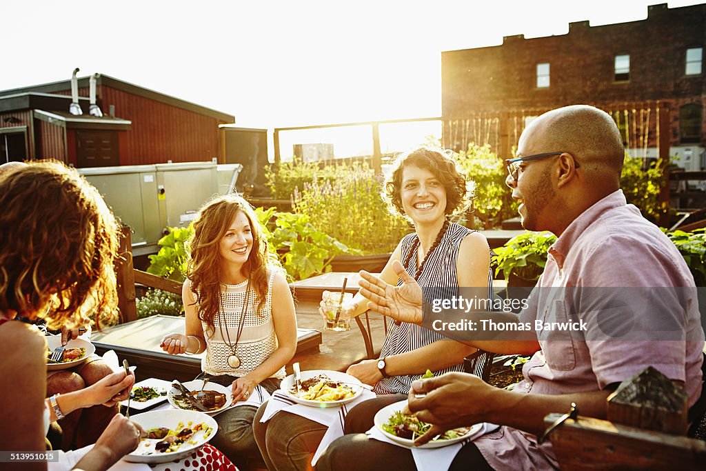 Laughing group of friends dining in rooftop garden