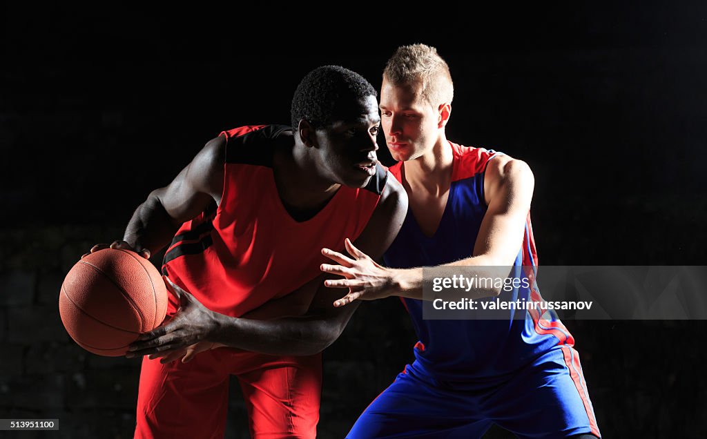 Caucasian and african basketball players on black background