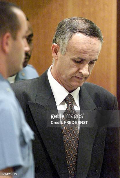 Bosnian Serb General Radislav Krstic holds his head down, closely watched by a United Nations security guard, as he enters the courtroom at the...