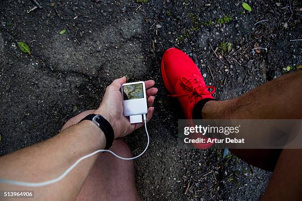 man running and checking from personal point of view his mp3 player with earphones and wearing a red trainers in the road asphalt. - adrenaline junkie stock pictures, royalty-free photos & images