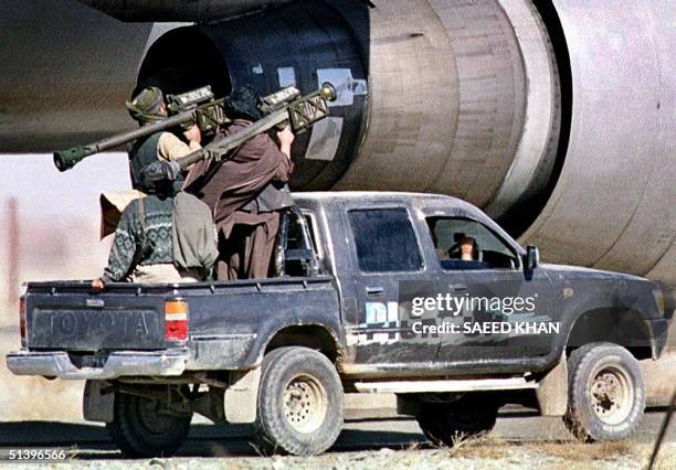 Taliban Islamic militia commandos riding on a pickup truck pass an engine of the hijacked Indian Airlines plane with US made heat seeking surface to...