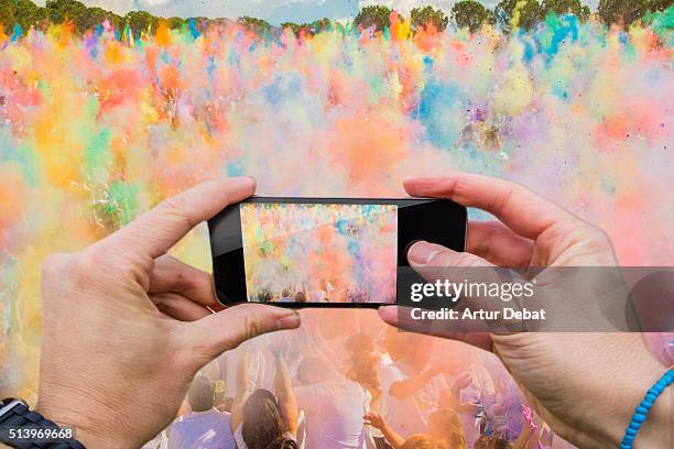 man taking pictures from personal point of view with smartphone during the colorful celebration of the holi festival with colorful powder. - powder throw fotografías e imágenes de stock