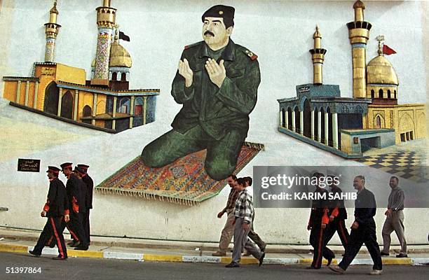 Iraqis pass a mural showing President Saddam Hussein praying in front of Iraq's two main Shiite Muslim mosques of Karbala near the Iraqi-Iranian...