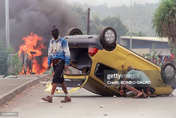 Hooded demonstrator walks away from a burning and overturned car, 06 September 1995, outside the Papeete's Faaa airport. Police used tear gas to...