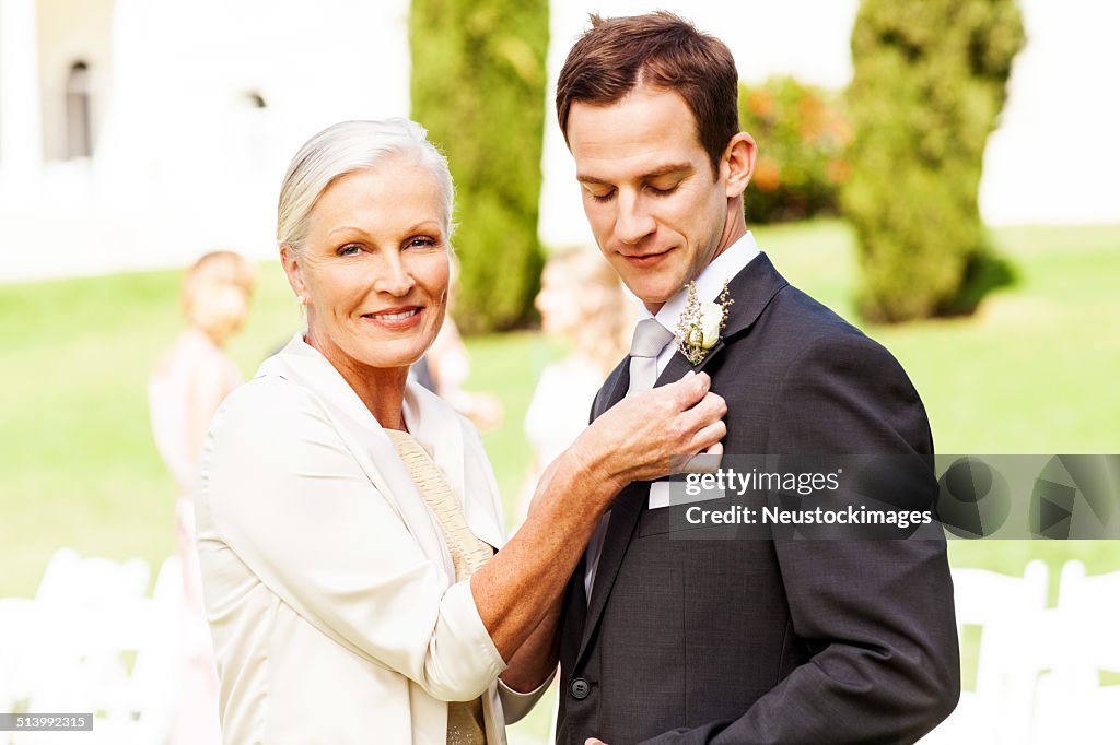 Mother Pinning Corsage On Groom's Suit At Outdoor Wedding