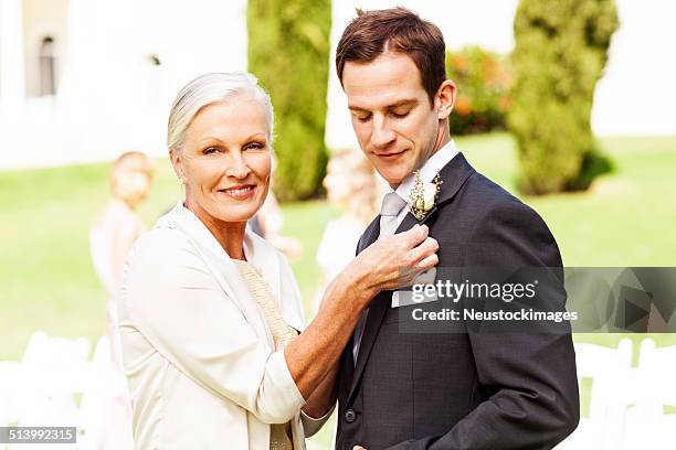 mother pinning corsage on groom's suit at outdoor wedding - bruidegom stockfoto's en -beelden
