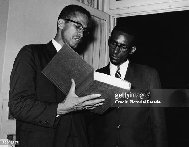 American Civil Rights activist and former Black Muslim leader Malcolm X holds an open copy of the Koran as he speaks to an unidentified man at...