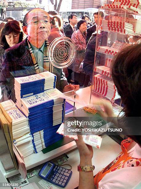 Japanese customer gazes at a female bank clerk counting lottery tickets to sell for 300 million yen Year-end Jumbo Lottery at a Tokyo lottery ticket...