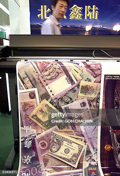 Technician waits as a poster of various currencies rolls out from a printer at the advertising material and equipment exhibition in Beijing 02 August...