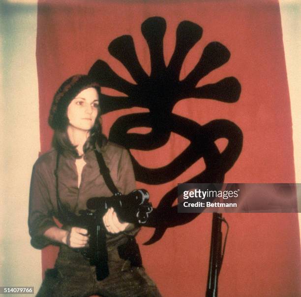 Portrait of American heiress Patty Hearst as she poses with a machine gun in front of a Symbionese Liberation Army flag, 1974