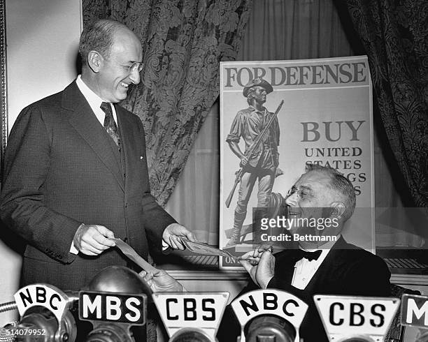 President Franklin Roosevelt buys the first of the U.S. Government's Defense Savings Bonds, from his Treasury Secretary Henry Morgenthau. FDR called...