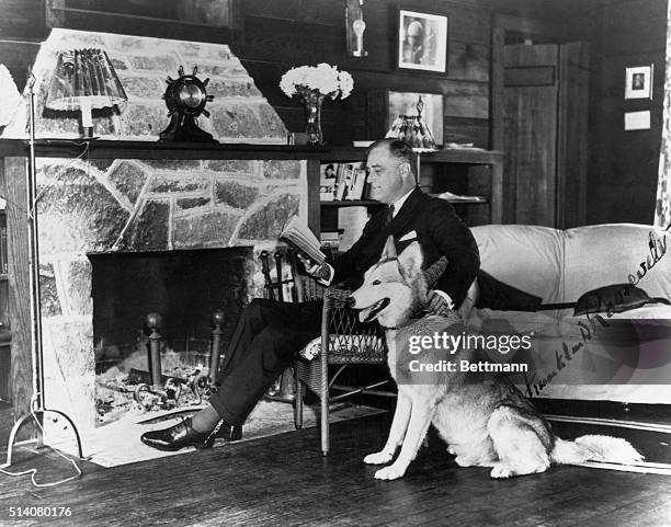 Franklin Delano Roosevelt pets his dog while reading beside the fireplace.