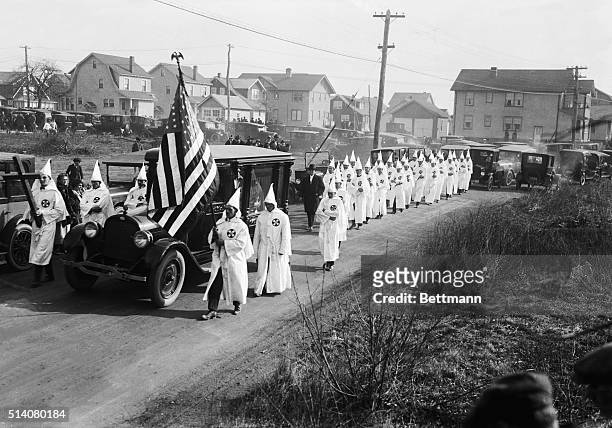 Ku Klux Klansmen march next to a hearse carrying one of their members.