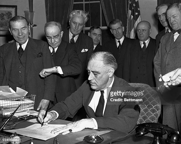 Cabinet members watch with mixed emotions as President Franklin D. Roosevelt, wearing a black armband, signs the United States' declaration of war...