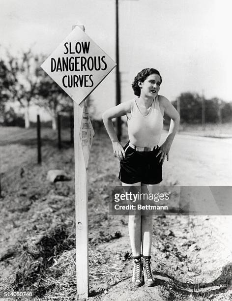 Attractive young woman standing next to a "Slow- Dangerous Curves" traffic sign.