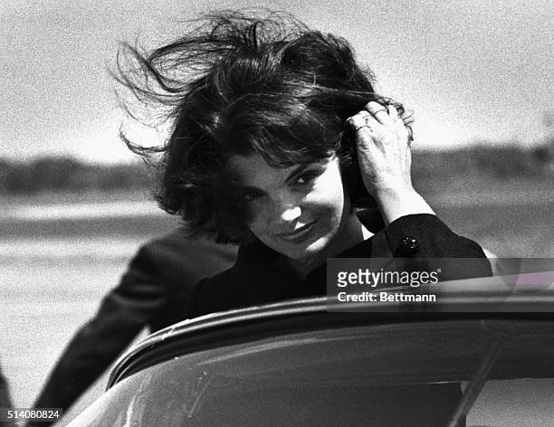 Jacqueline Kennedy brushes her wind-blown hair out of her eyes as she enters a car at Barnstable Airport in Hyannis. She arrived to appear in an...