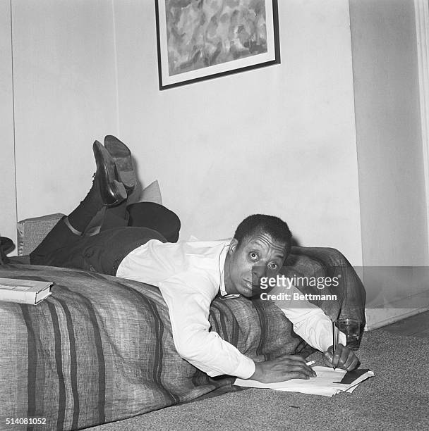 New York, NY: In a writing position that doesn't appear to be comfortable but really is, novelist James Baldwin sprawls across the bed in his New...