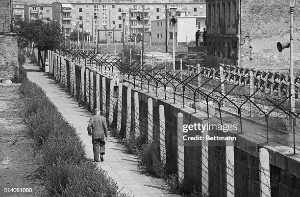 Man walks along the West Berlin side of the Berlin Wall in 1962. Rows of barbed wire on the eastern side are meant to discourage escape attempts.