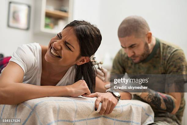 young woman experiencing pain while getting tattoo. - grimacing stock pictures, royalty-free photos & images