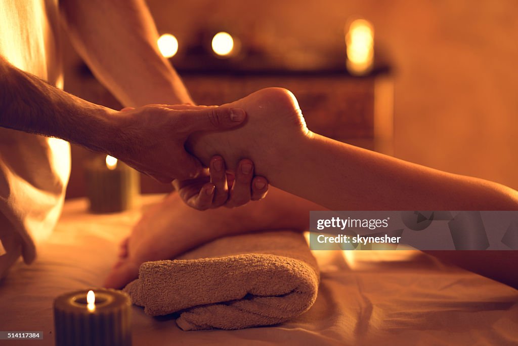 Unrecognizable massage therapist massaging woman's foot at spa.