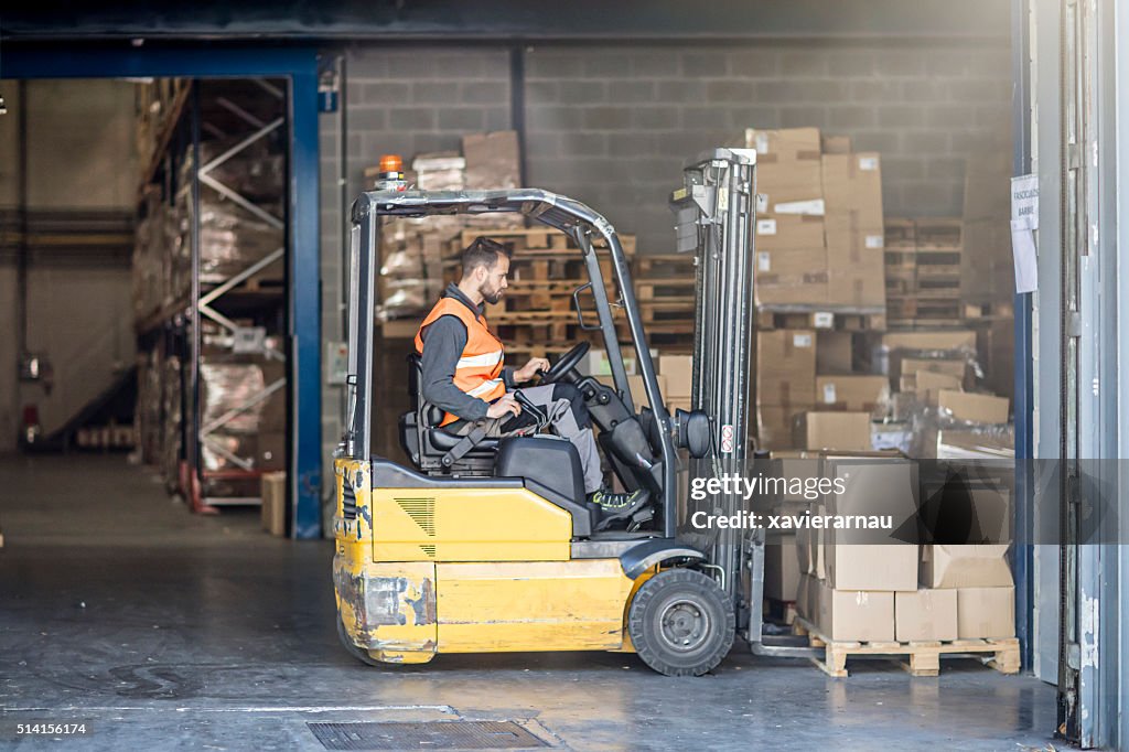 Worker driving forklift in warehouse