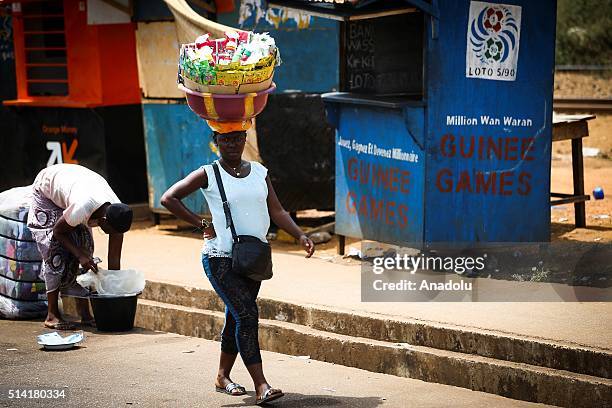 Guinean woman carries a bucket on her head as she tries to sell cleaning materials in Conakry, Guinea on March 7, 2016. Guinean women give their...