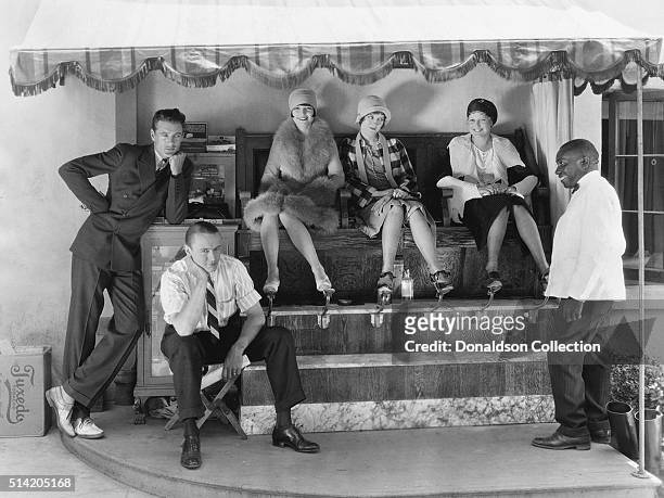 Actors Gary Cooper and Jack Luden wait for a shoe shine while actresses Louise Brooks, Doris Hill, and Thelma Todd get their shoes polished.