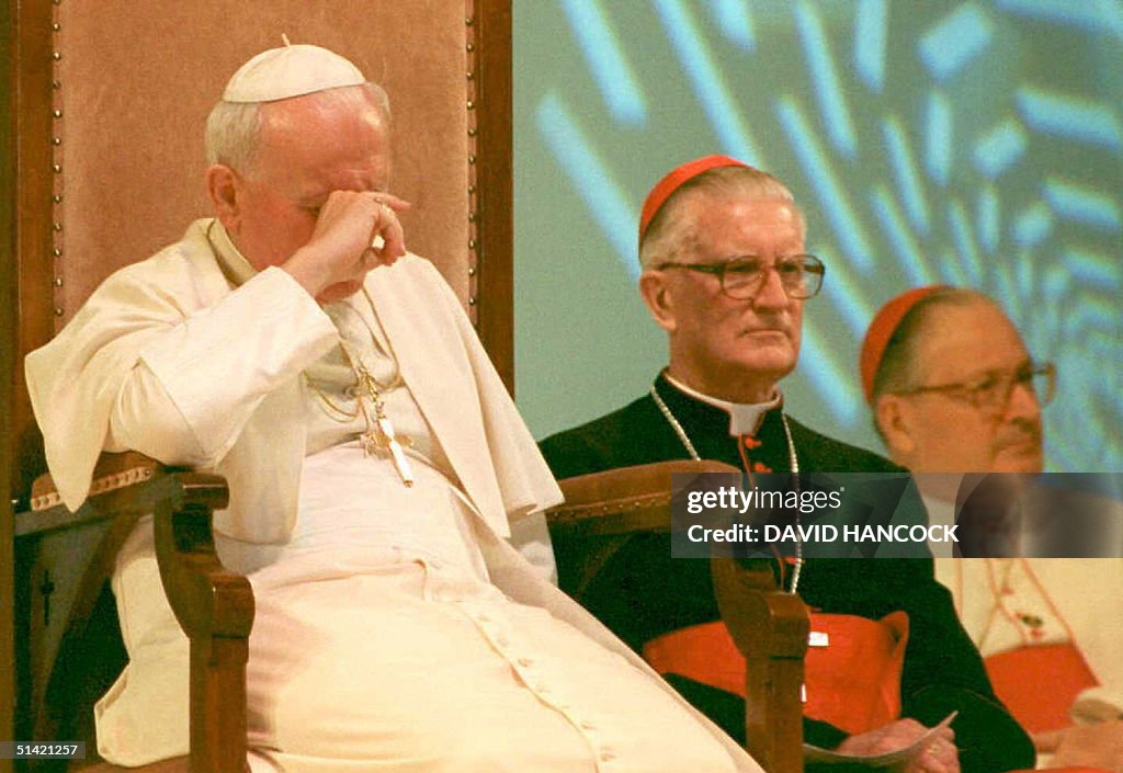 Pope John Paul II (L) rubs his eyes while sitting