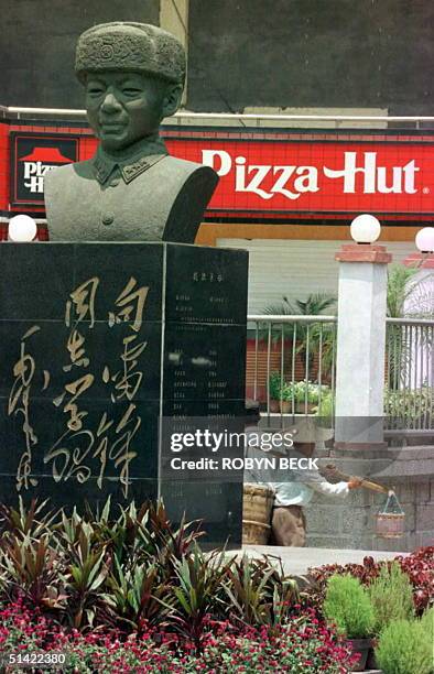 Peddlar passes between a statue of Lei Feng, communist China's most famous model soldier, and a Pizza Hut restaurant 29 July in downtown Xiamen, one...