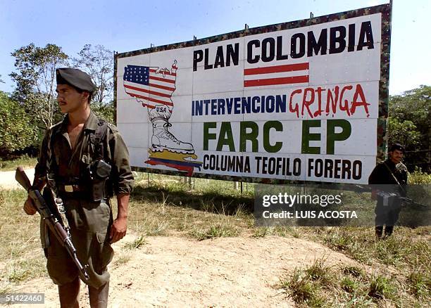 Two guerrillas of the Revolutionary Armed Forces of Colombia stand guard on a highway next to a billboard with propaganda against the US-backed...