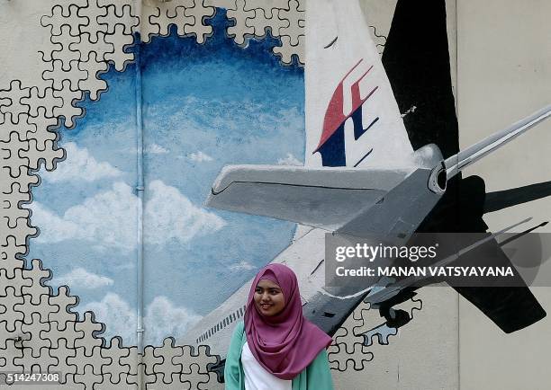 Malaysian woman poses in front of a mural of missing Malaysia Airlines MH370 plane in a back-alley in Shah Alam on March 8, 2016. Malaysia and...