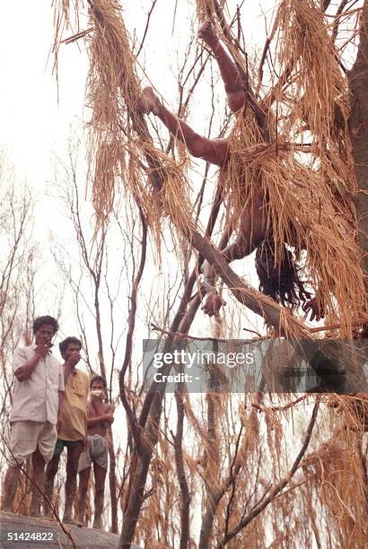 Photo taken 03 May 1991 shows people covering their noses to protect themselves from the stnch of a dead body hanging from a tree near Hatya, in the...