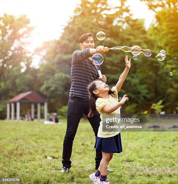 padre e hija divirtiéndose en el parque con las burbujas de jabón - bubbles happy fotografías e imágenes de stock