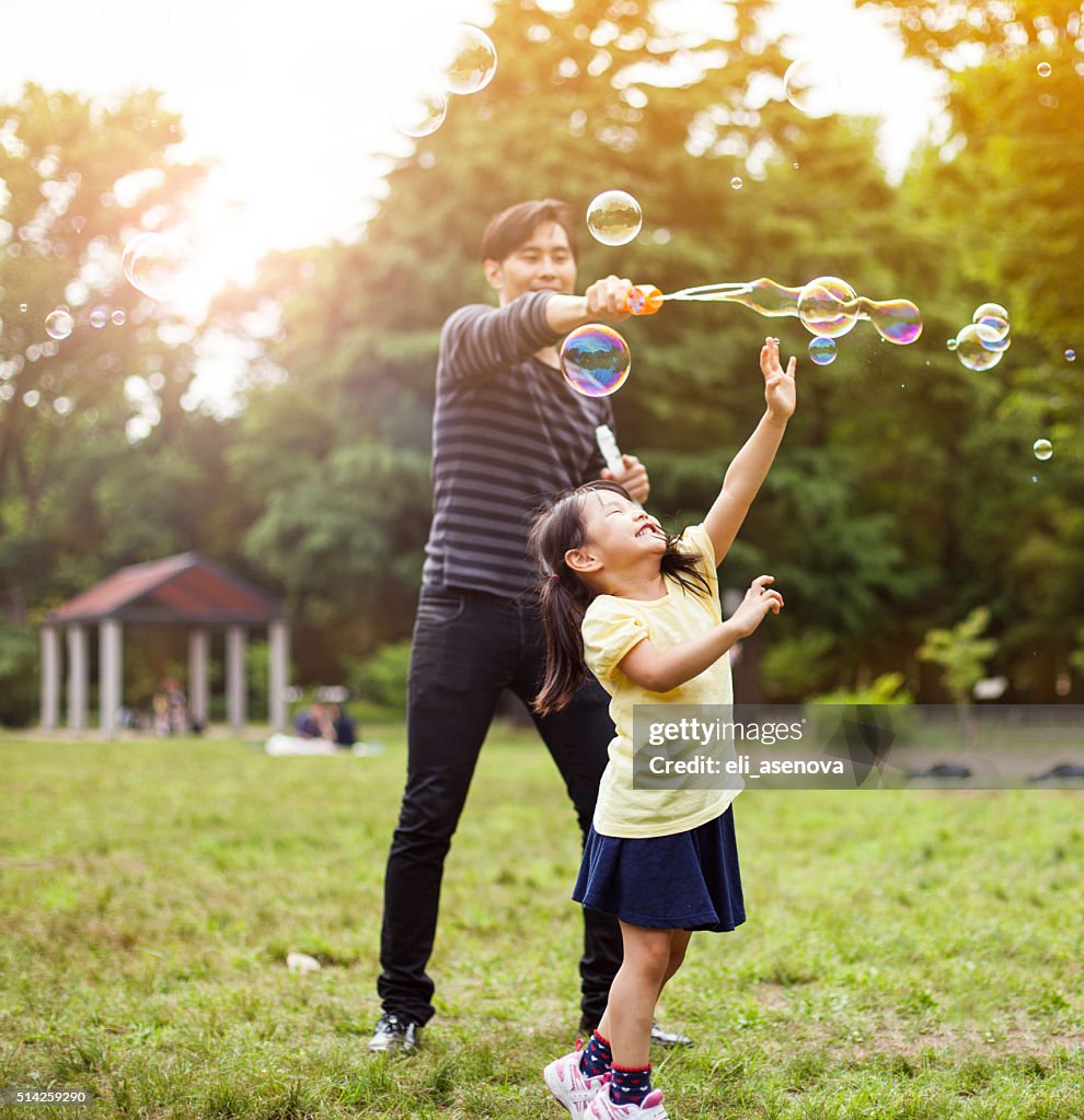 Father and daughter having fun in park with Soap Bubbles