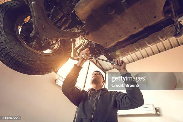 below view of young mechanic repairing a chassis of car. - chassis stockfoto's en -beelden