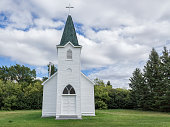 little white country church with steeple surrounded by green trees.