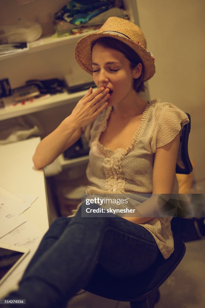 Tired clothing designer yawning in fashion design studio.