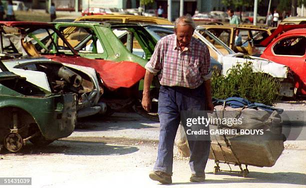 Bosnian man pulls his belongings on a luggage trolley 23 August 1993 as he walks past a parking lot full of car wrecks, on Alipasino Polje Avenue,...