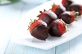 Fresh strawberries dipped in dark chocolate on blue wooden backg