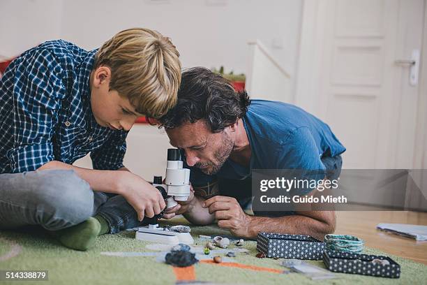 father and son using microscope at home. - leanincollection father stock-fotos und bilder