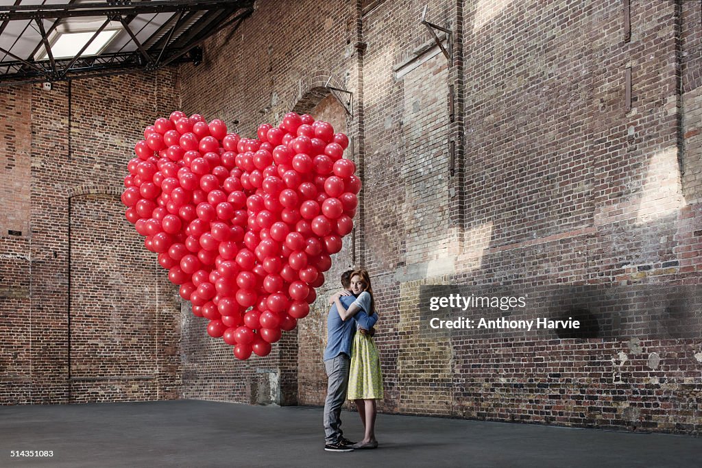 Couple in warehouse with heart made of balloons