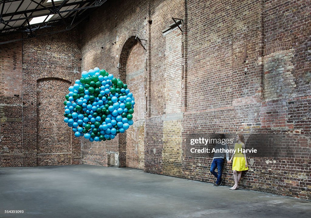 Couple in warehouse with globe made of balloons