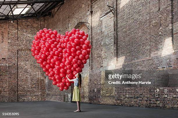 woman in warehouse with heart made of balloons - amar fotografías e imágenes de stock