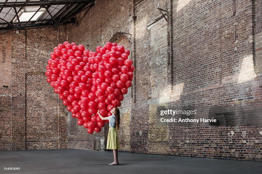 Woman in warehouse with heart made of balloons