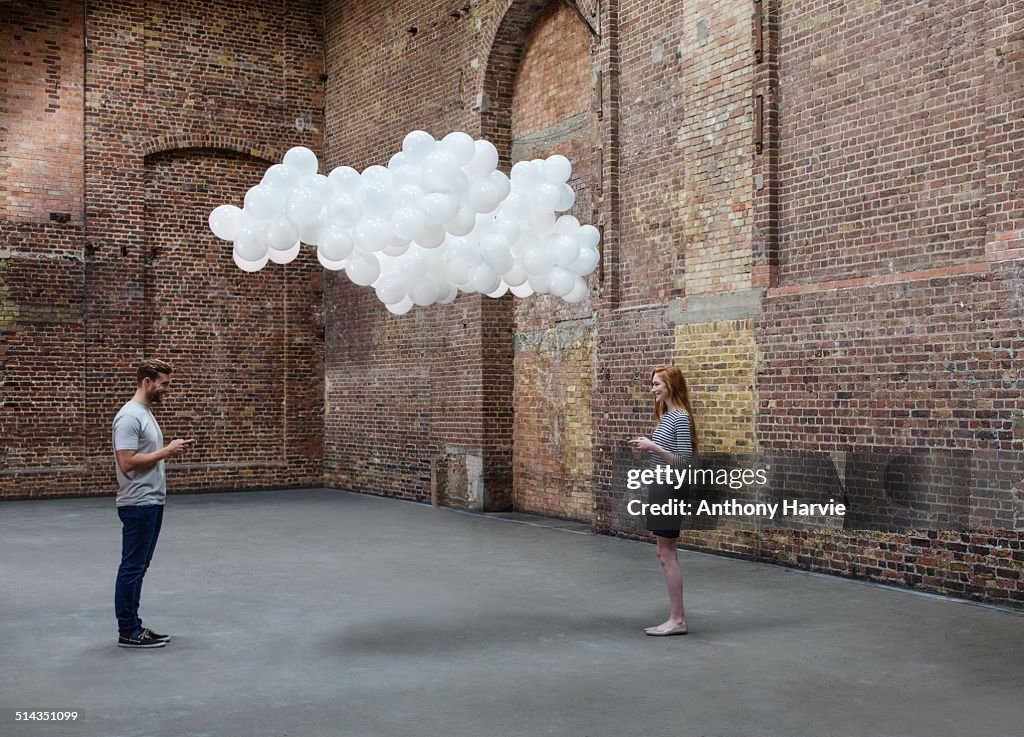 Couple in warehouse, cloud of balloons above heads