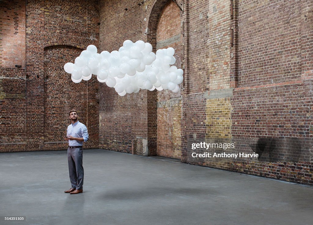 Man in warehouse with cloud of balloons above head
