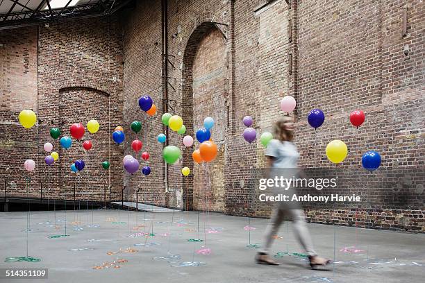 woman walking in warehouse with colourful balloons - same people different clothes - fotografias e filmes do acervo
